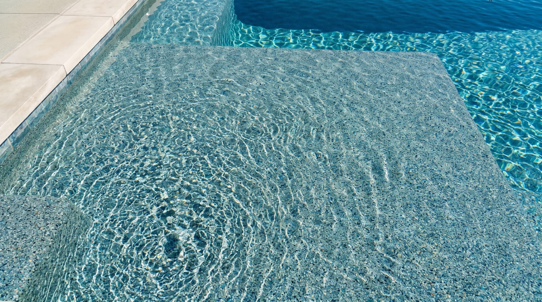 Close-up of a pebble pool finish with sunlight caustics, the most common remodel surface upgrade and the visual signal that a tired pool has been brought back