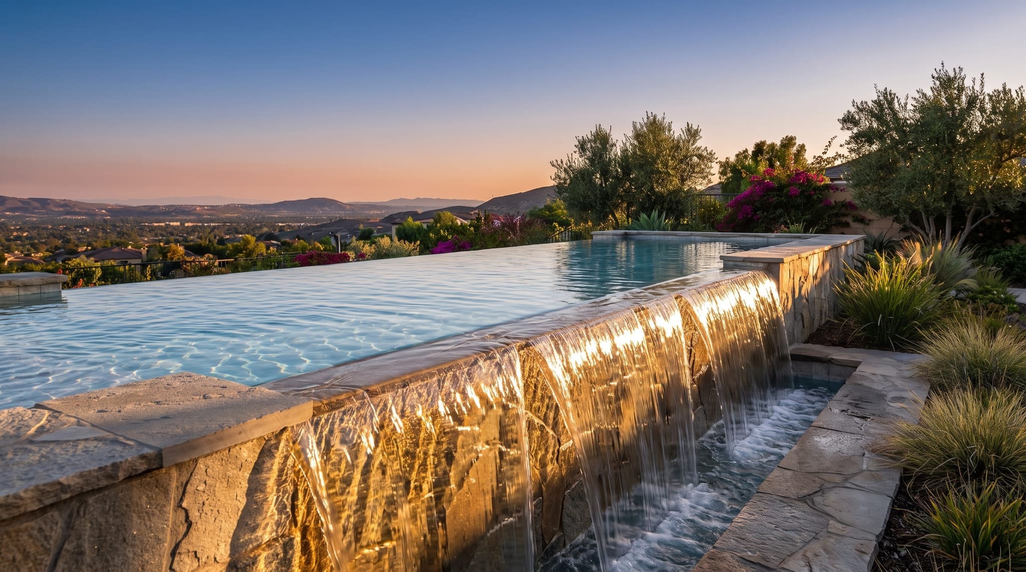 Tight horizontal close-up of a vanishing-edge weir at sunset, water flowing over the spillway lip in a continuous thin sheet that catches the orange sky, hazy Inland Empire valley dropping away below